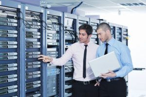 Two young men pointing to server rack
